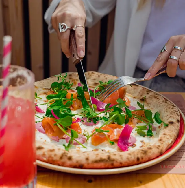 Femme qui est en train de couper une pizza avec ses couverts
